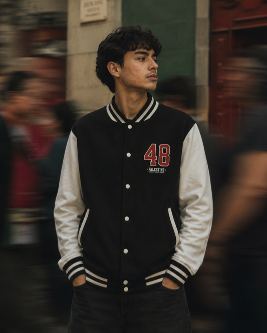 Man wearing a 1948 Palestine Heavyweight Letterman Jacket by Warrior Ink Apparel on a blurred street background